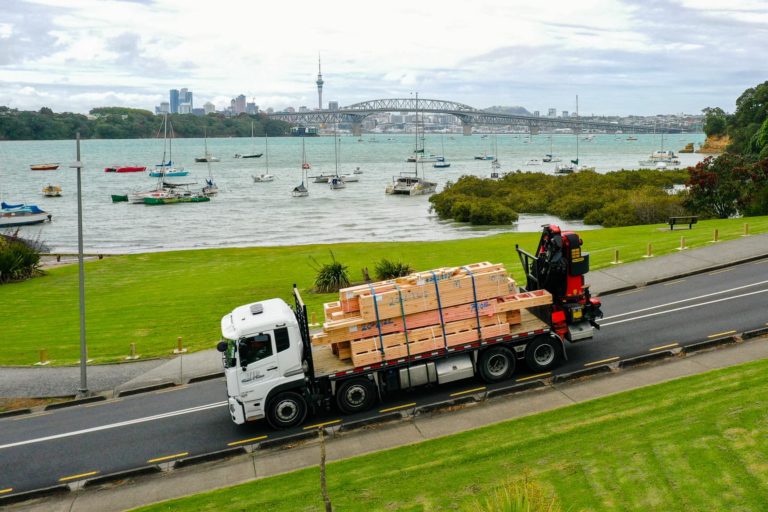 VIP Frames & Trusses crane truck transporting timber framing with Auckland harbour and Harbour Bridge in the background